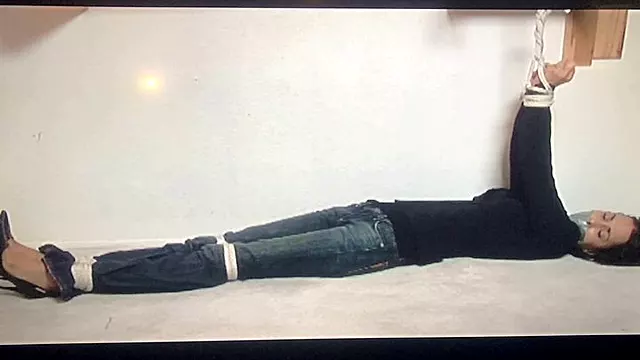 Tape-gagged brunette Gia Mancini lay stretched out and writhing on the floor with her arms tied overhead to a wooden bar!