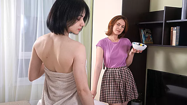 Two slim, short-haired lesbians share a sex toy in their room