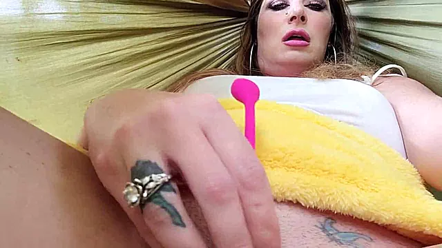 Big-titted MILF masturbates with a dildo in a hammock outdoors.