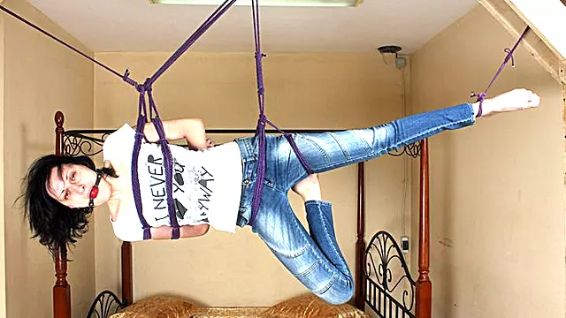 Ballgagged barefoot Ola in white t-shirt and blue jeans, suspended with violet hemp rope sideways, is tickled by camera man (HD WMV)